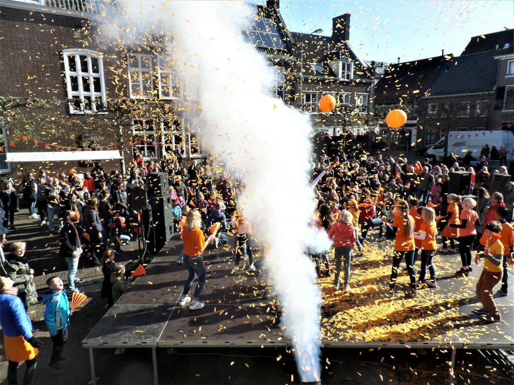 Koningsdag op de markt met mensen in oranje t-shirts en oranje ballonen