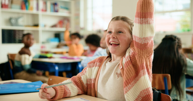 Een vrolijk meisje dat haar hand opsteekt in de klas